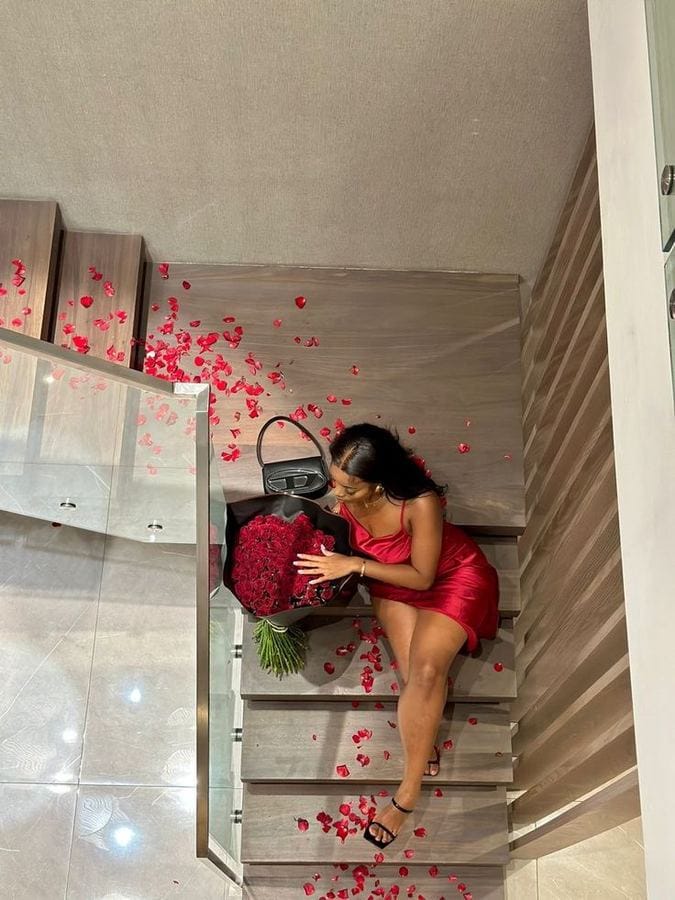 A woman in red with a bouquet of red roses among rose petals